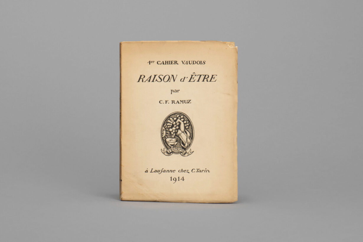 The image shows the cover of the first Cahier Vaudois, entitled “Raison d’être par C.F. Ramuz.” Below the title is an oval emblem showing a hand squeezing a bunch of grapes, the juice flowing into a wine glass, with a banner reading “J'exprime” (“I express”). Below, it reads: “à Lausanne chez C. Tarin. 1914.”