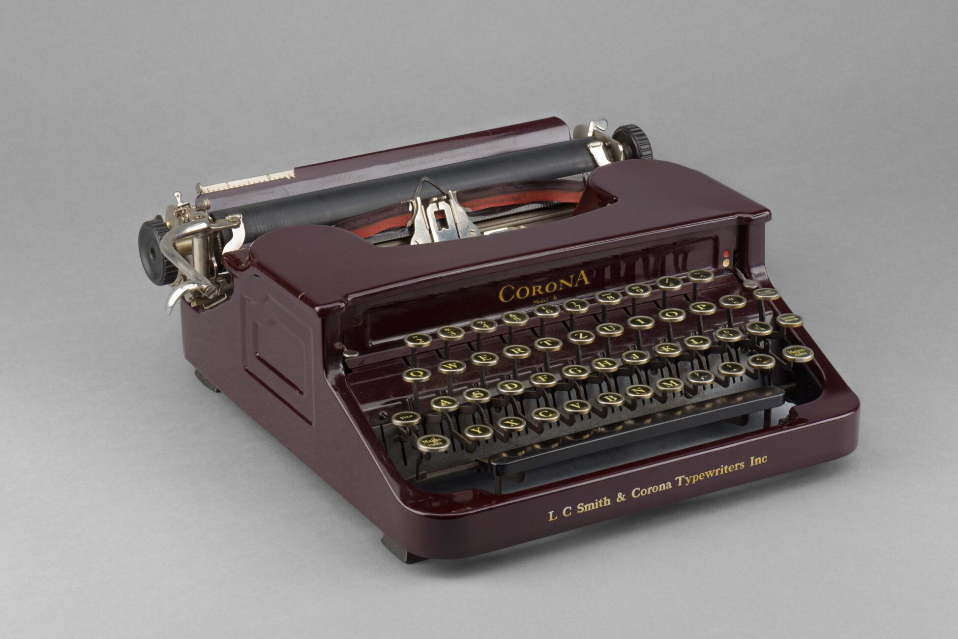 The picture shows a typewriter that belonged to C.F. Ramuz. The machine is burgundy-colored and its brand name, Corona, is written in gold above the keys.