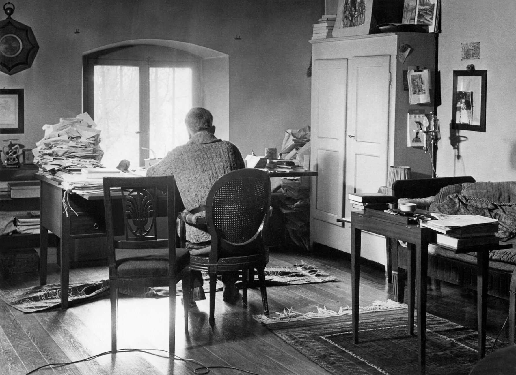 Photo noir blanc de Ramuz de dos, assis à son bureau en train d’écrire. Le plan est large.